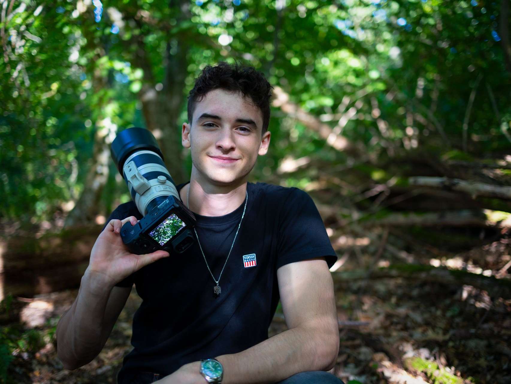 Portrait of wildlife photographer Denat Lahi, with a camera and telephoto lens in a forest enviroment,