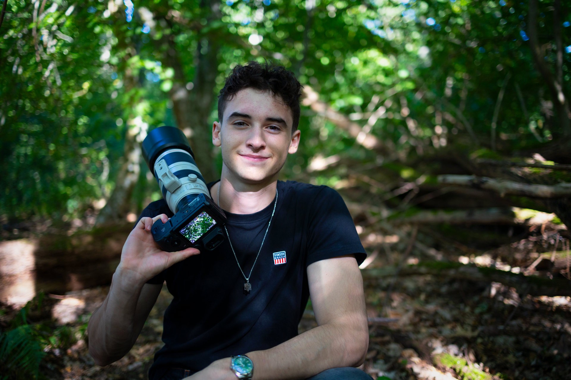 Portrait of wildlife photographer Denat Lahi, with a camera and telephoto lens in a forest enviroment,